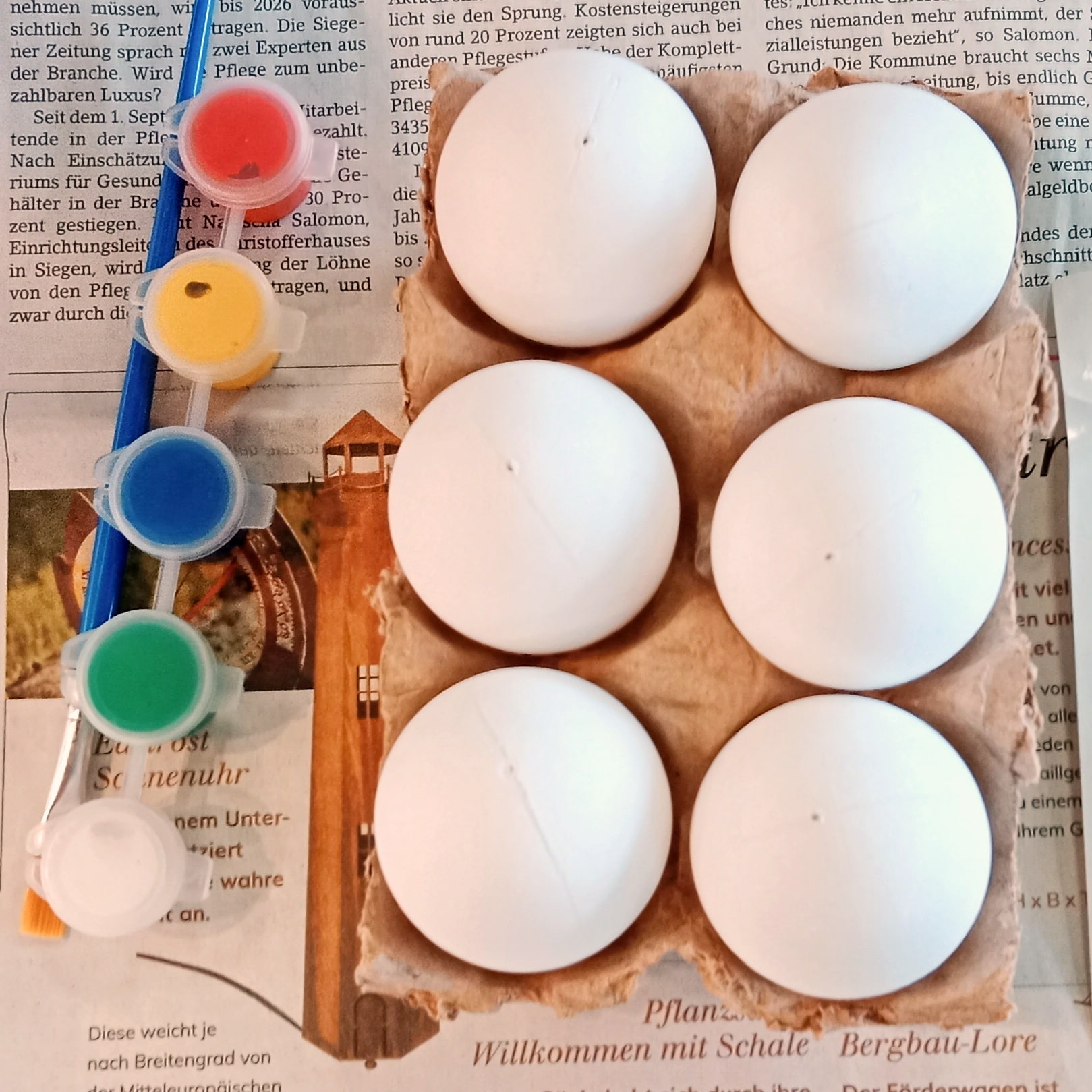 Ein Karton mit weißen Eiern und mehrere Behälter Acrylfarbe stehen bereit
