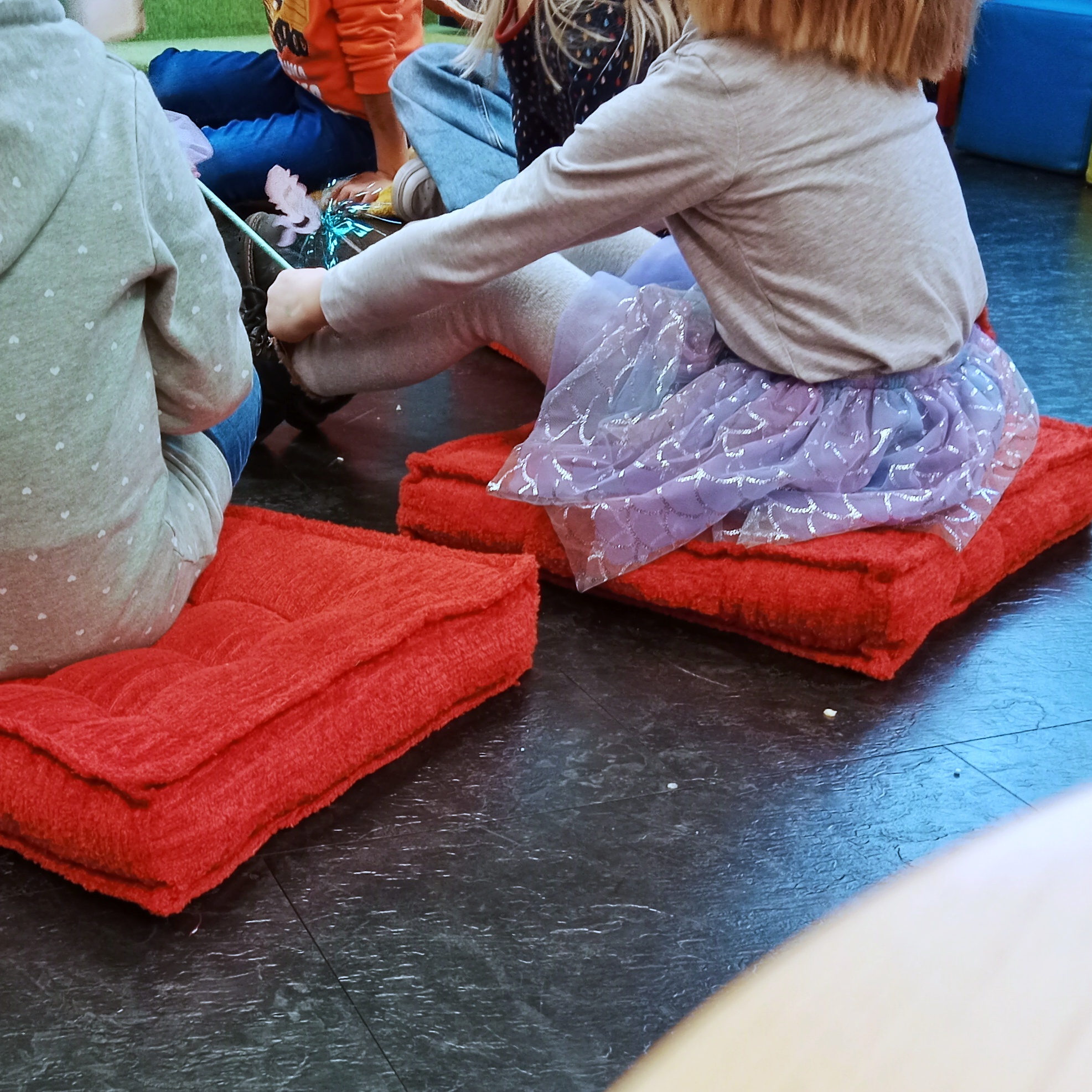 Kinder sitzen gespannt auf Bodenkissen.