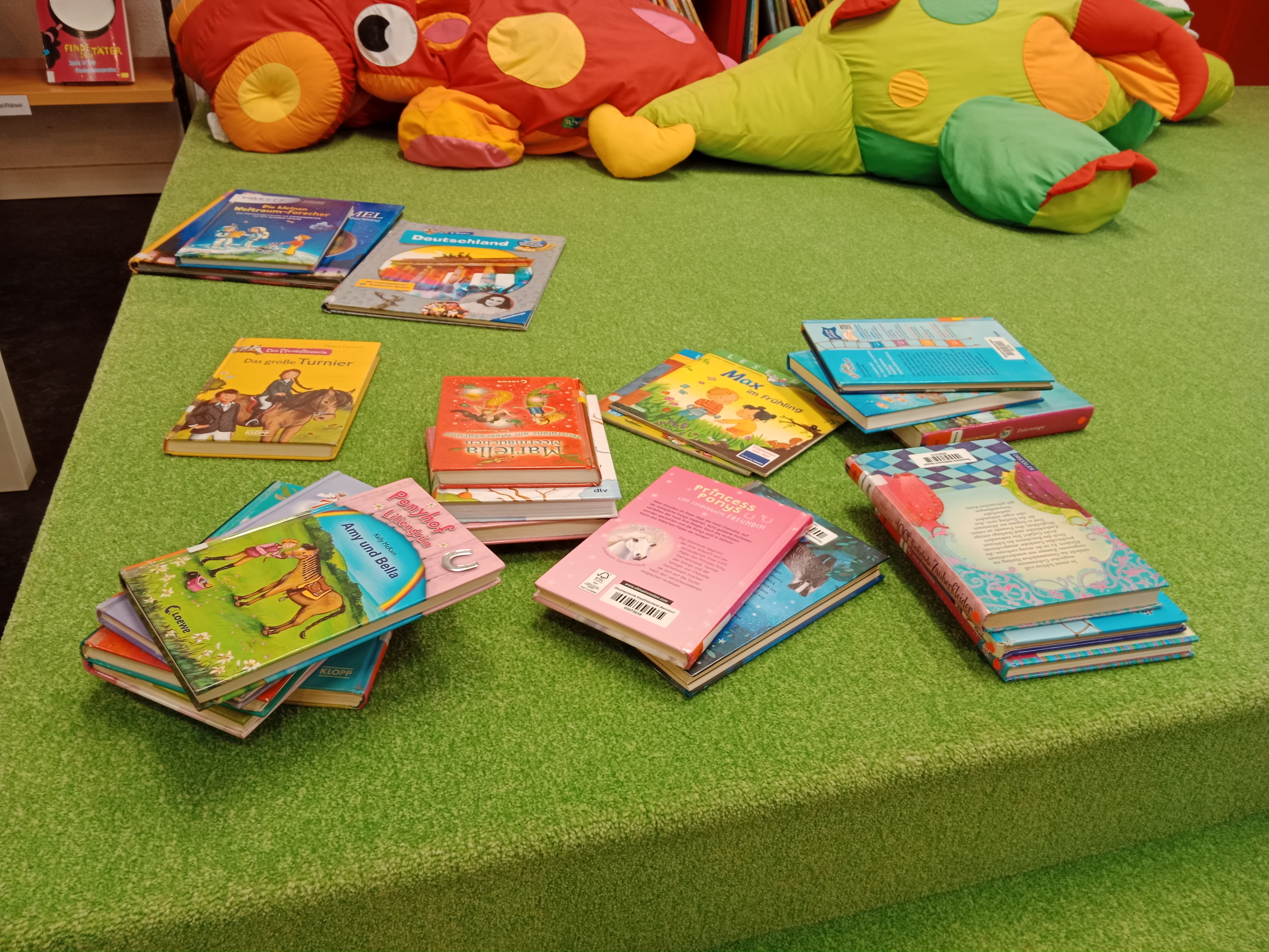 Mehrere Stapel Kinderbücher auf einem grünen Teppich.